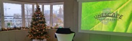 Helles Büro dekoriert für Weihnachten mit einem Blick auf die Stadt, daneben eine Präsentation zum Thema 'Unescape Project Earth', nachhaltige Initiativen
