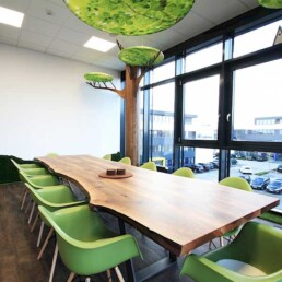 Innovativer Besprechungsraum mit einem langen Holztisch und grünen Stühlen, naturnahe Gestaltung mit künstlichen Baumkronen an der Decke in Münster